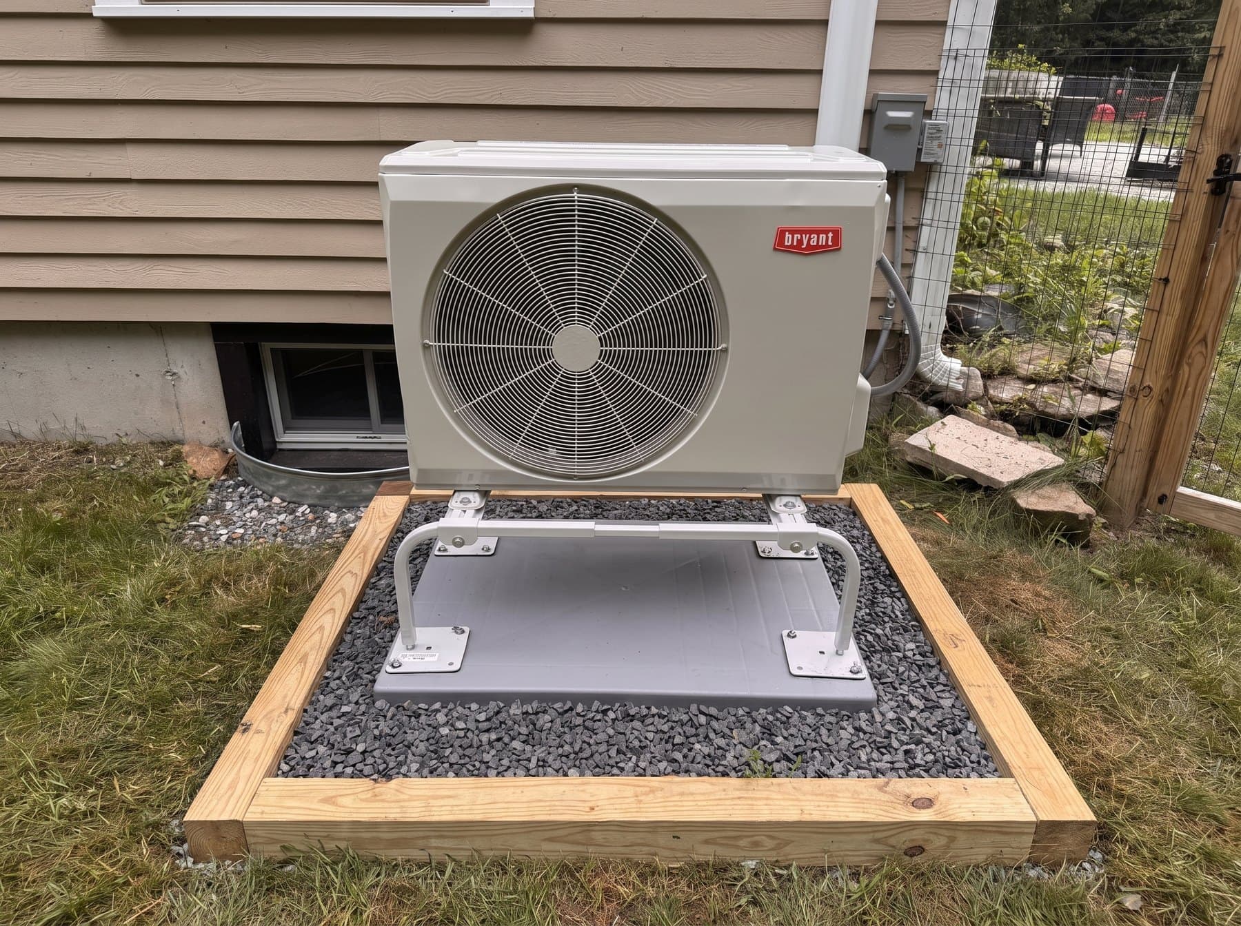 Bryant outdoor unit on a framed, gravel-set pad beside a home